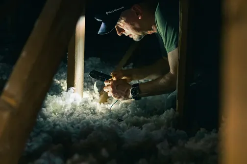 Man wearing a head torch inspects white loft insulation between wooden joists